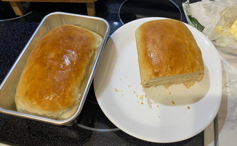 Freshly baked Amish milk bread loaf with golden, buttery crust—one sliced to show soft, fluffy interior.